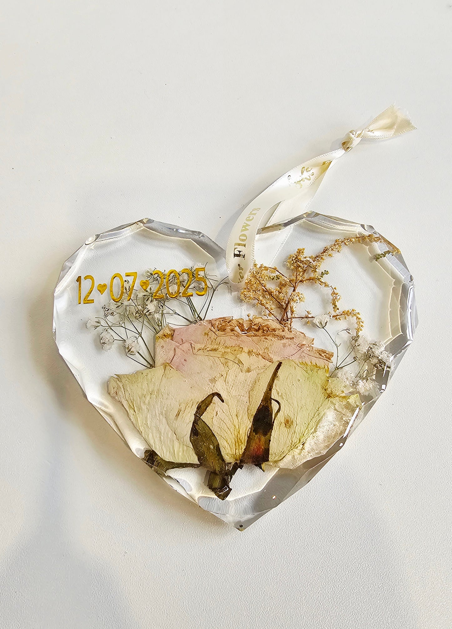 Heart-shaped decorative resin heart with dried flowers, a butterfly, and a date on a light background