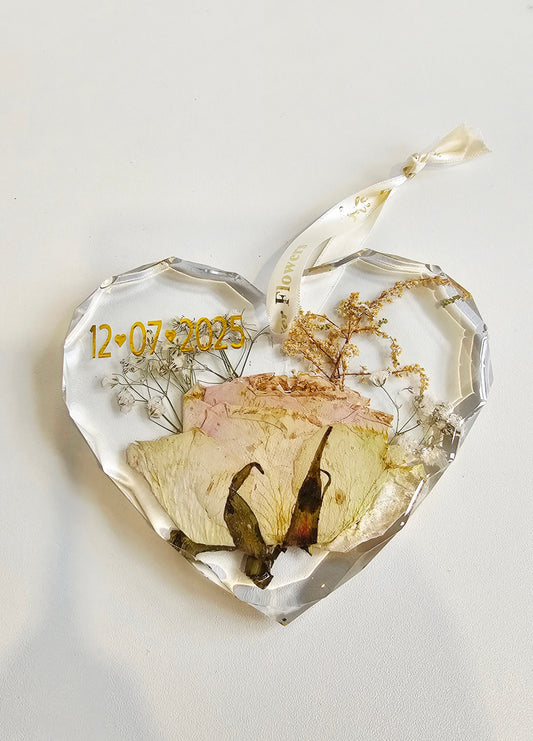 Heart-shaped decorative resin heart with dried flowers, a butterfly, and a date on a light background