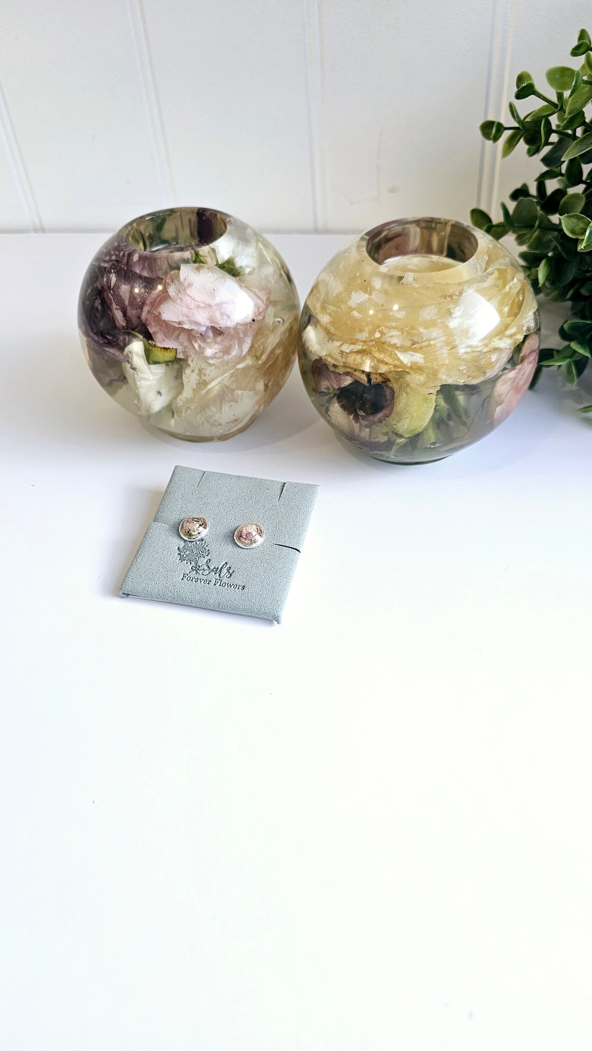 Two floral resin ball tealight holders  and a pair of earrings on a white surface with a plant in the background.