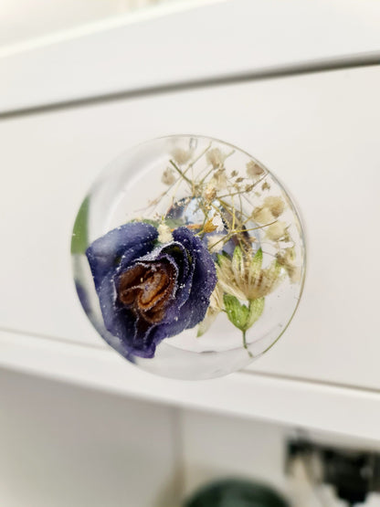 Round decorative resin drawer handle a purple flower and green leaves on a white surface