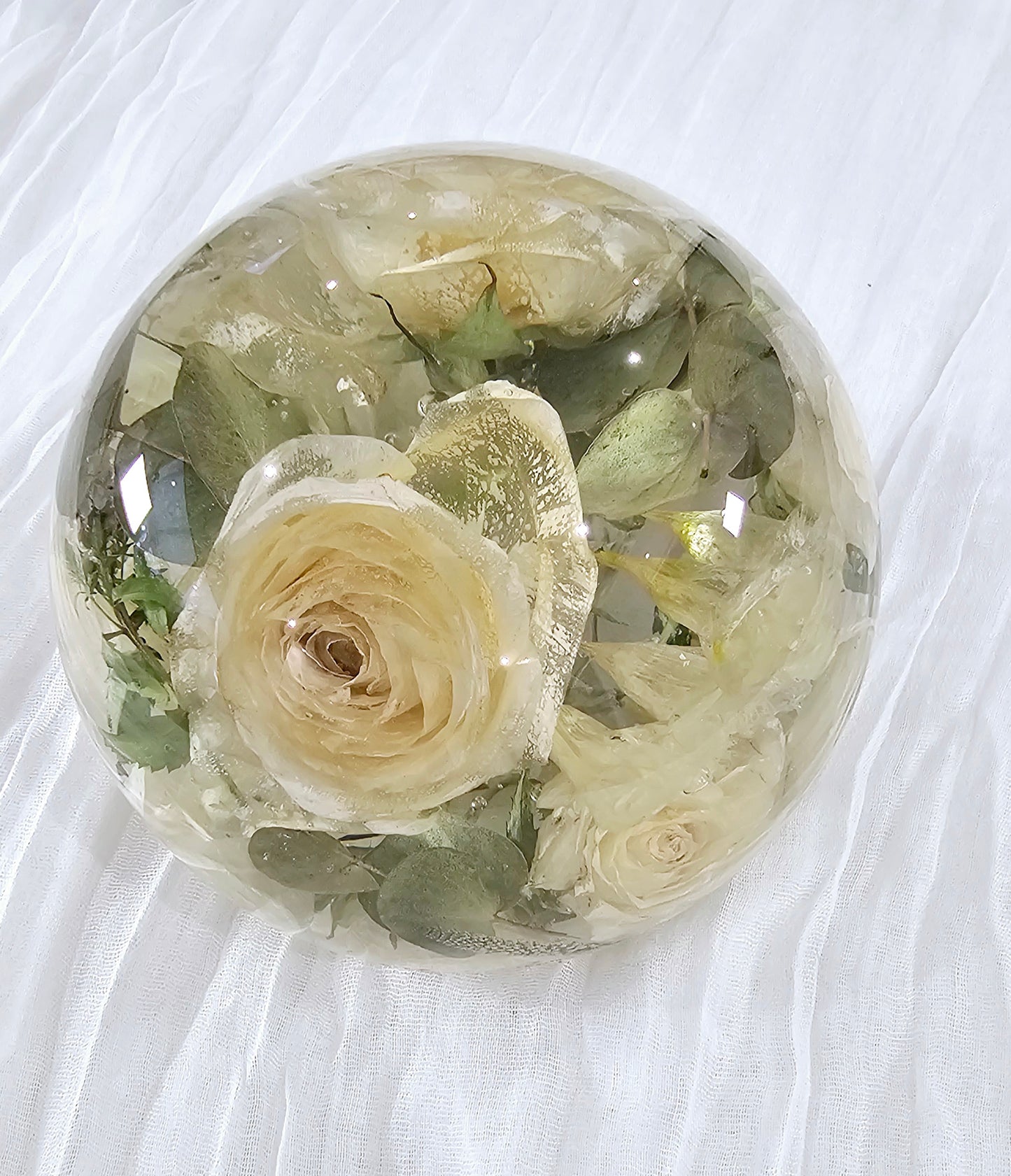 Round transparent resin sphere with preserved wedding flowers on a white fabric background side view