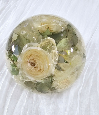 Round transparent resin sphere with preserved wedding flowers on a white fabric background side view
