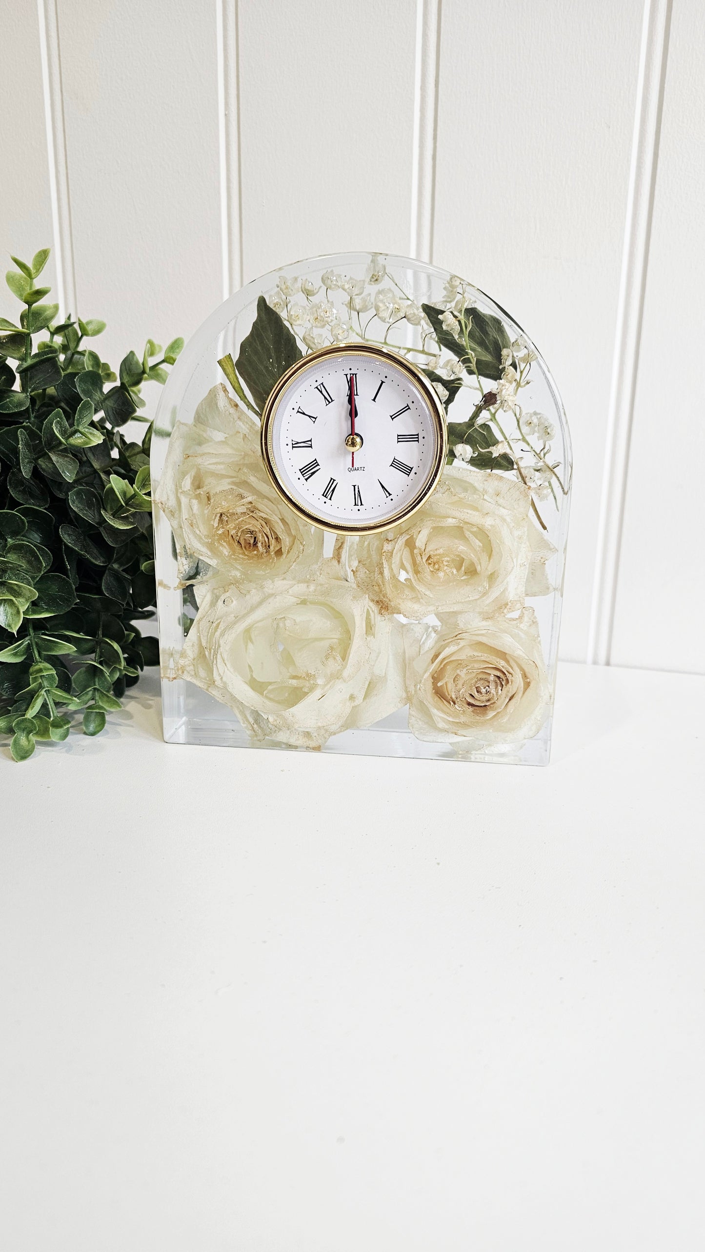 Decorative clock with white roses in a clear glass block on a white surface.