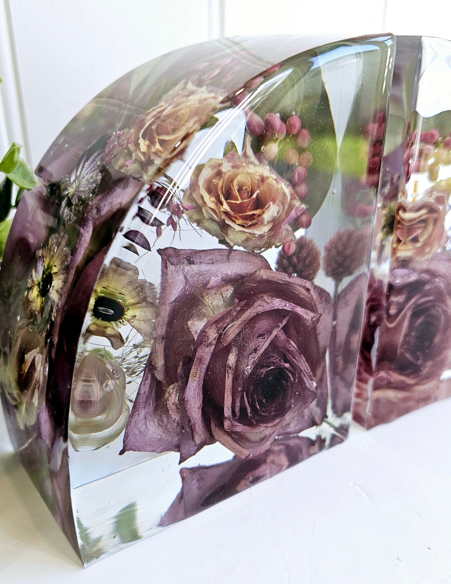 Clear resin bookends with preserved flowers including roses on a white surface