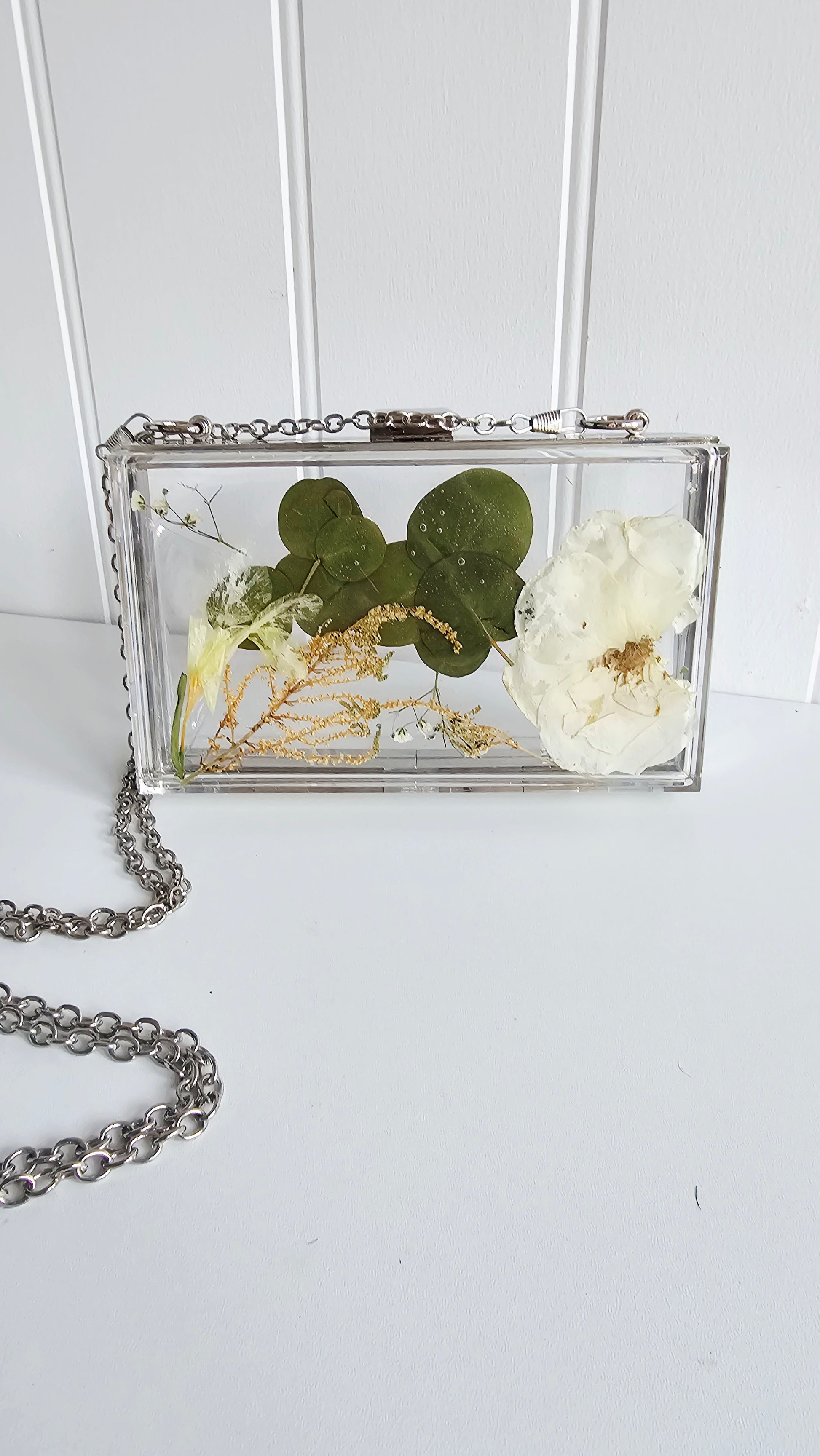 Clear clutch with pressed flowers and chain on a white background