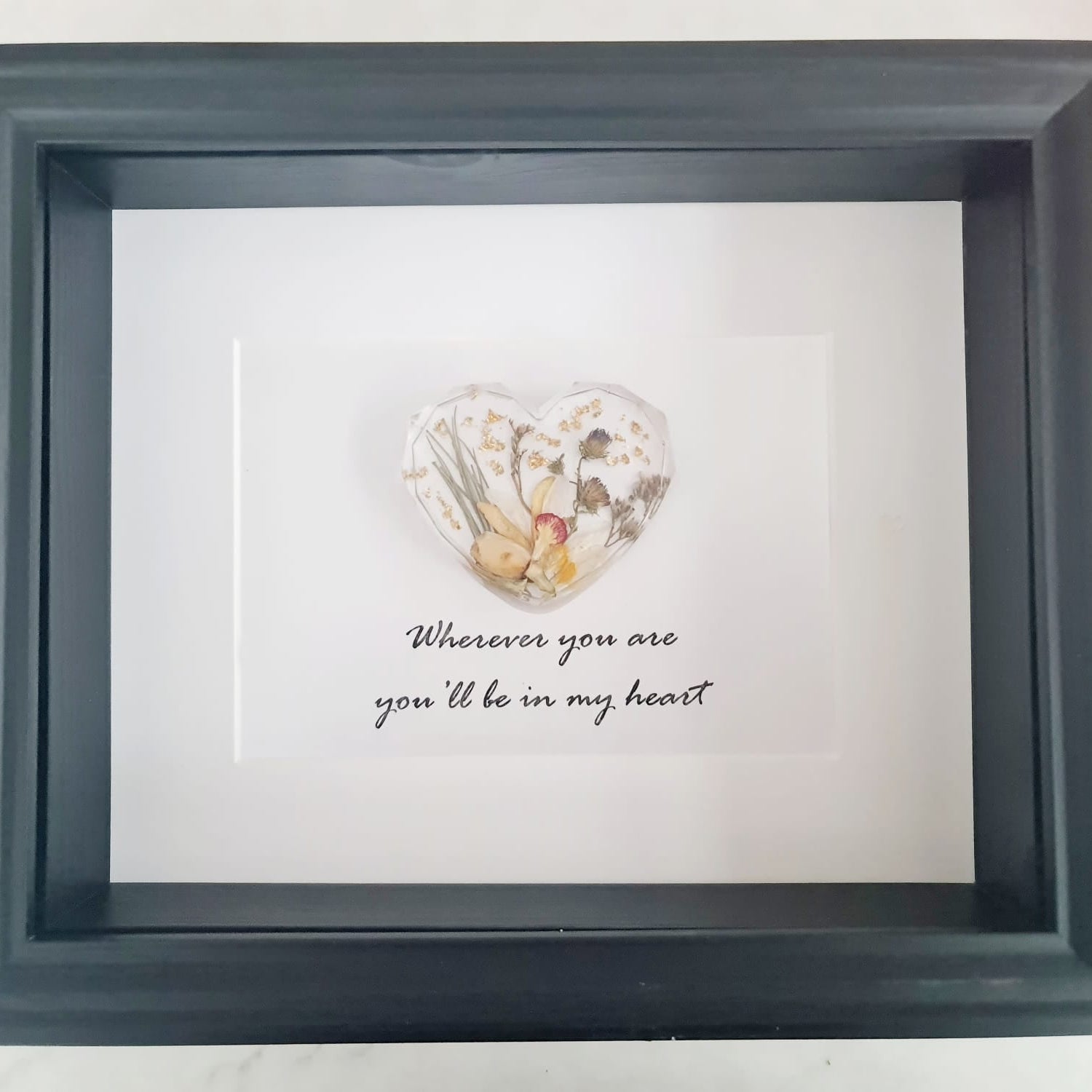 Framed artwork with a heart-shaped arrangement of sresi and a quote on a white background