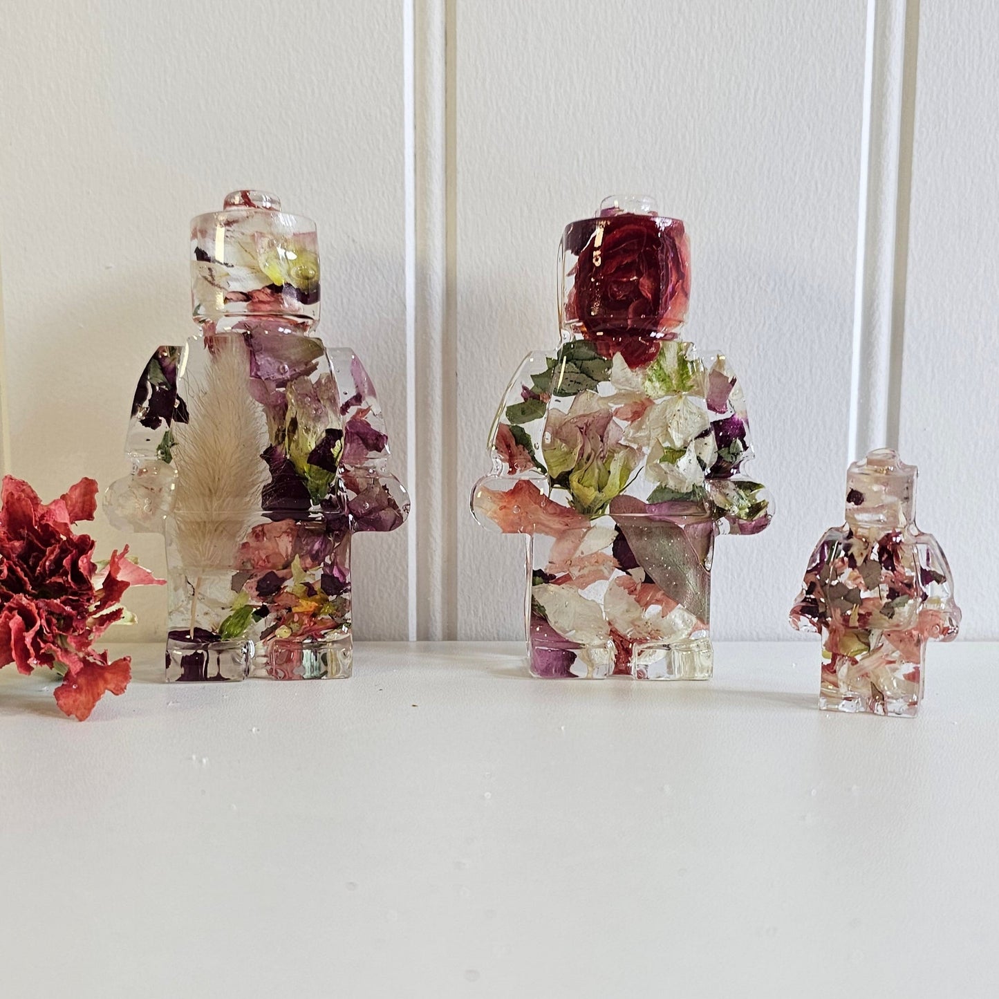Decorative resin lego men with floral arrangements on a white surface