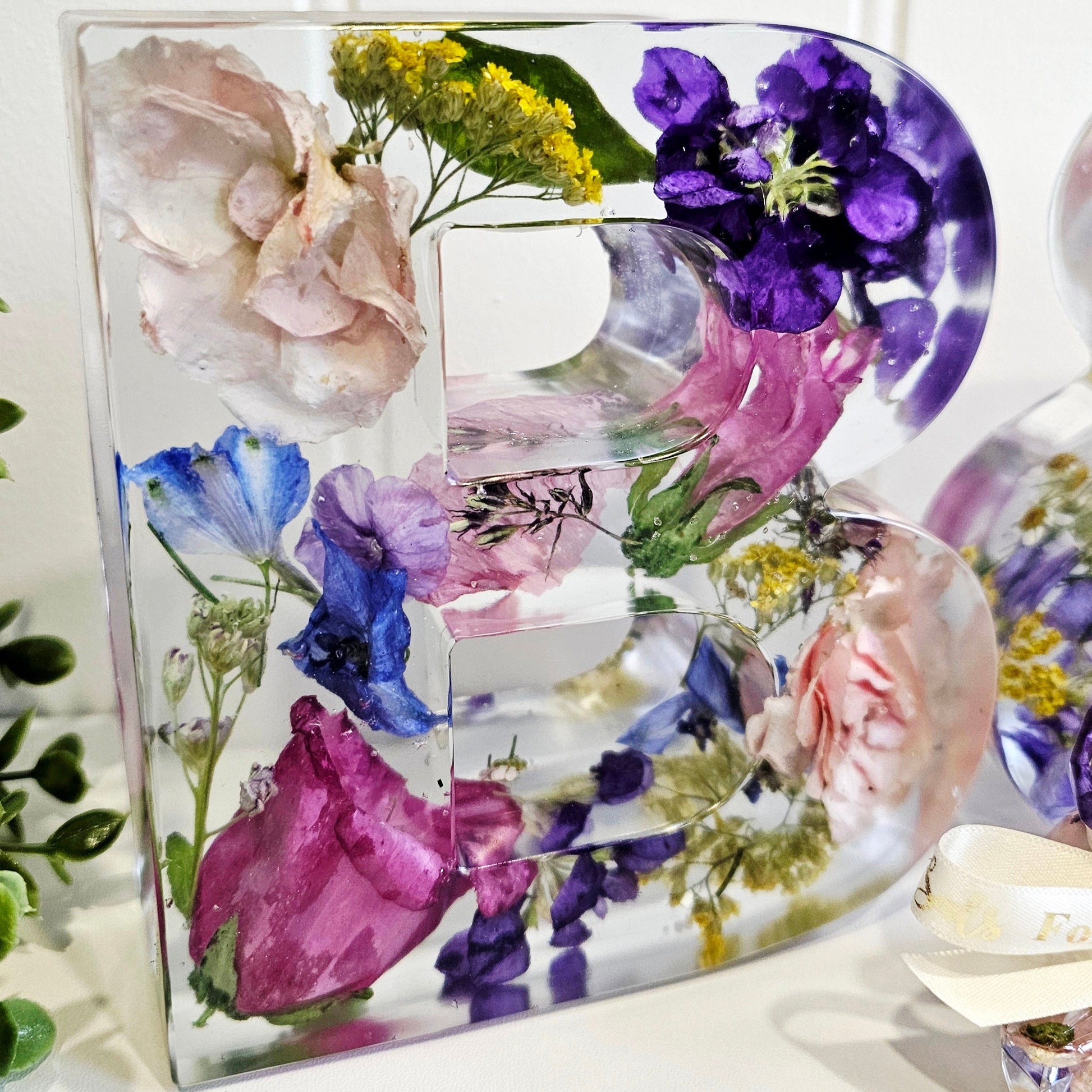 Decorative letter 'B' made of preserved flowers in resin on a white background front view
