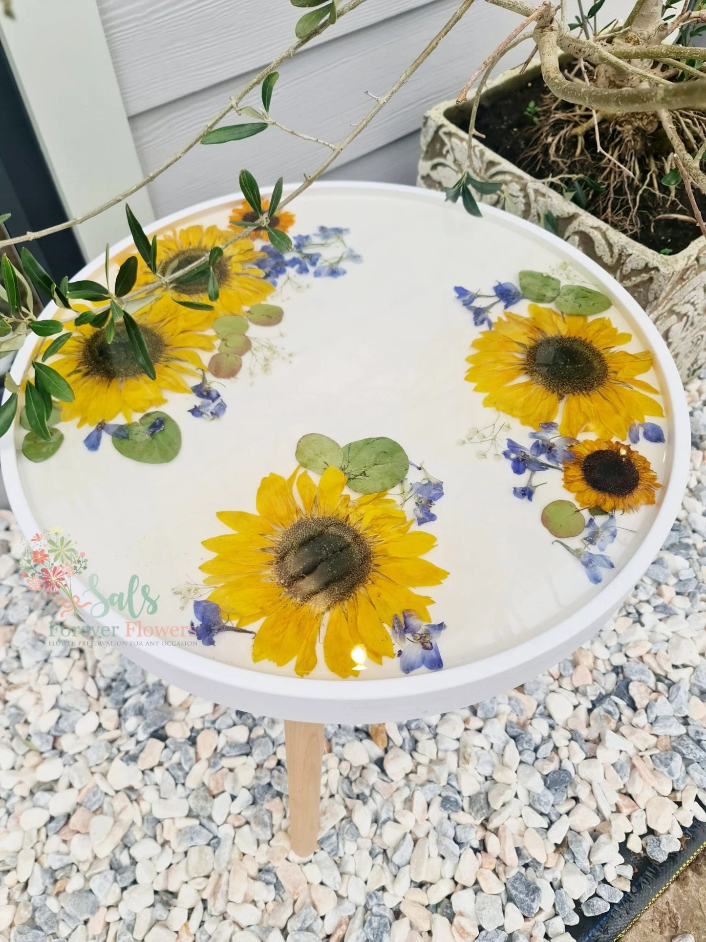 Decorative resin table with sunflowers and greenery on a pebbled surface