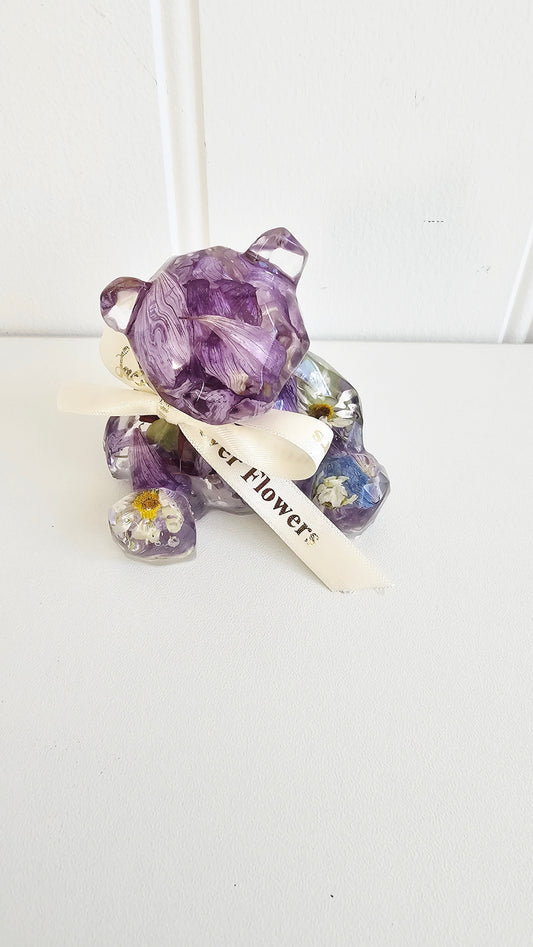 Decorative resin bear with purple cflowers and' text on a white background
