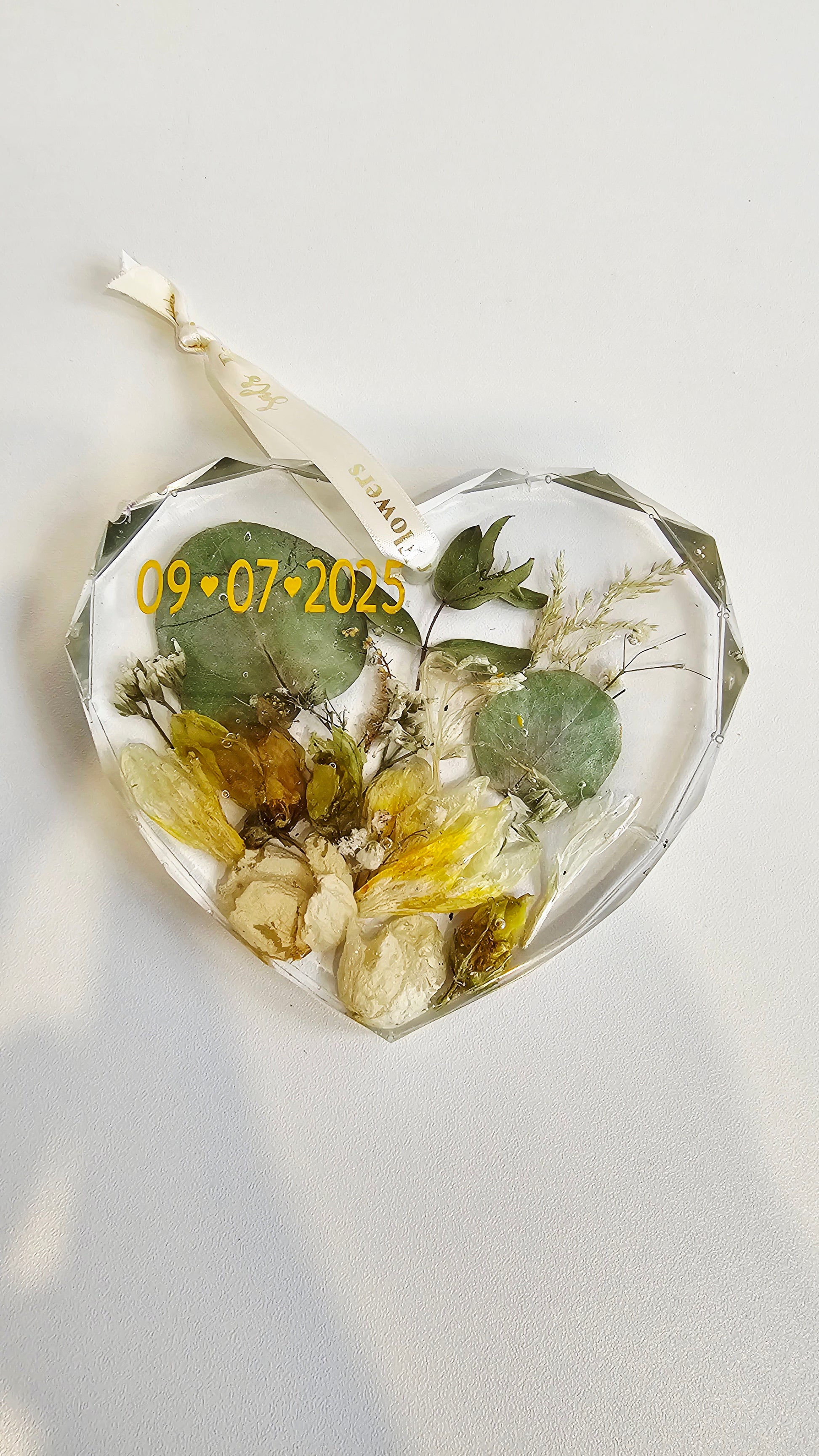 Heart-shaped resin ornament with pressed flowers and a date on a light background