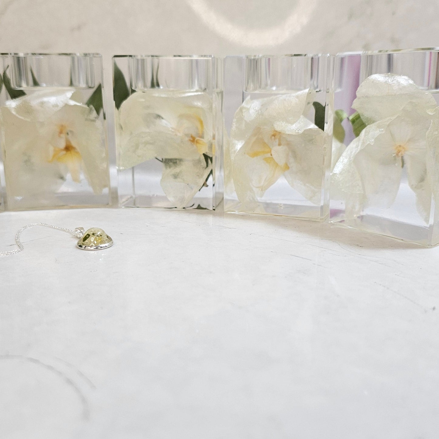 Four clear resin pillar tealight holders with white flowers on a white surface.