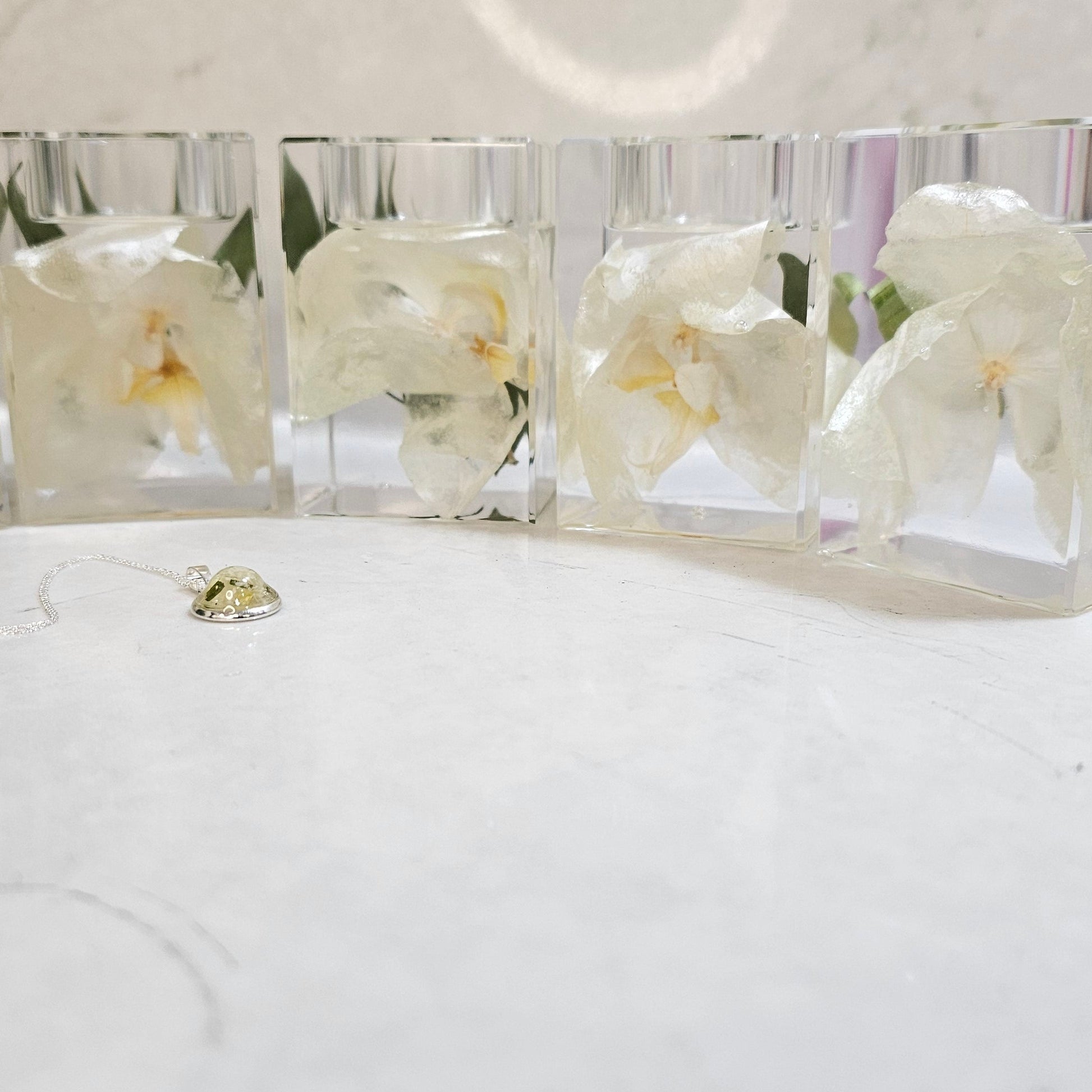 Four clear resin pillar tealight holders with white flowers on a white surface.