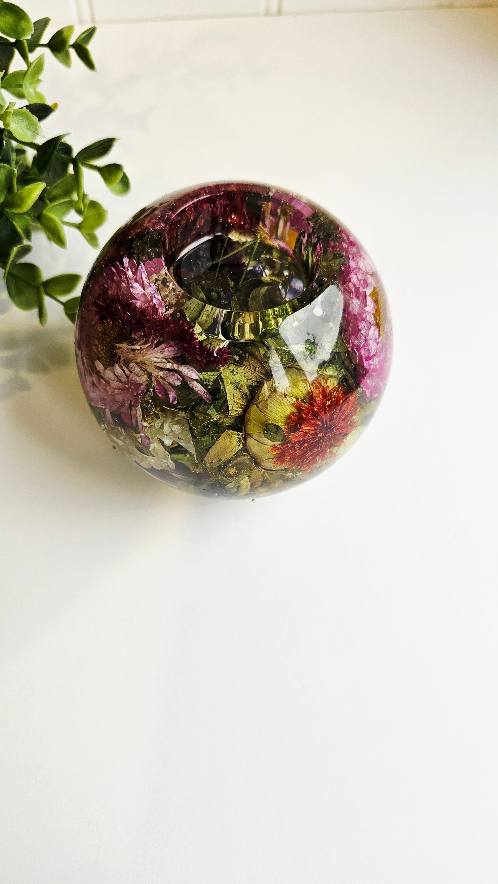 Round resin tealight holder with dried flowers on a white surface with a plant in the background