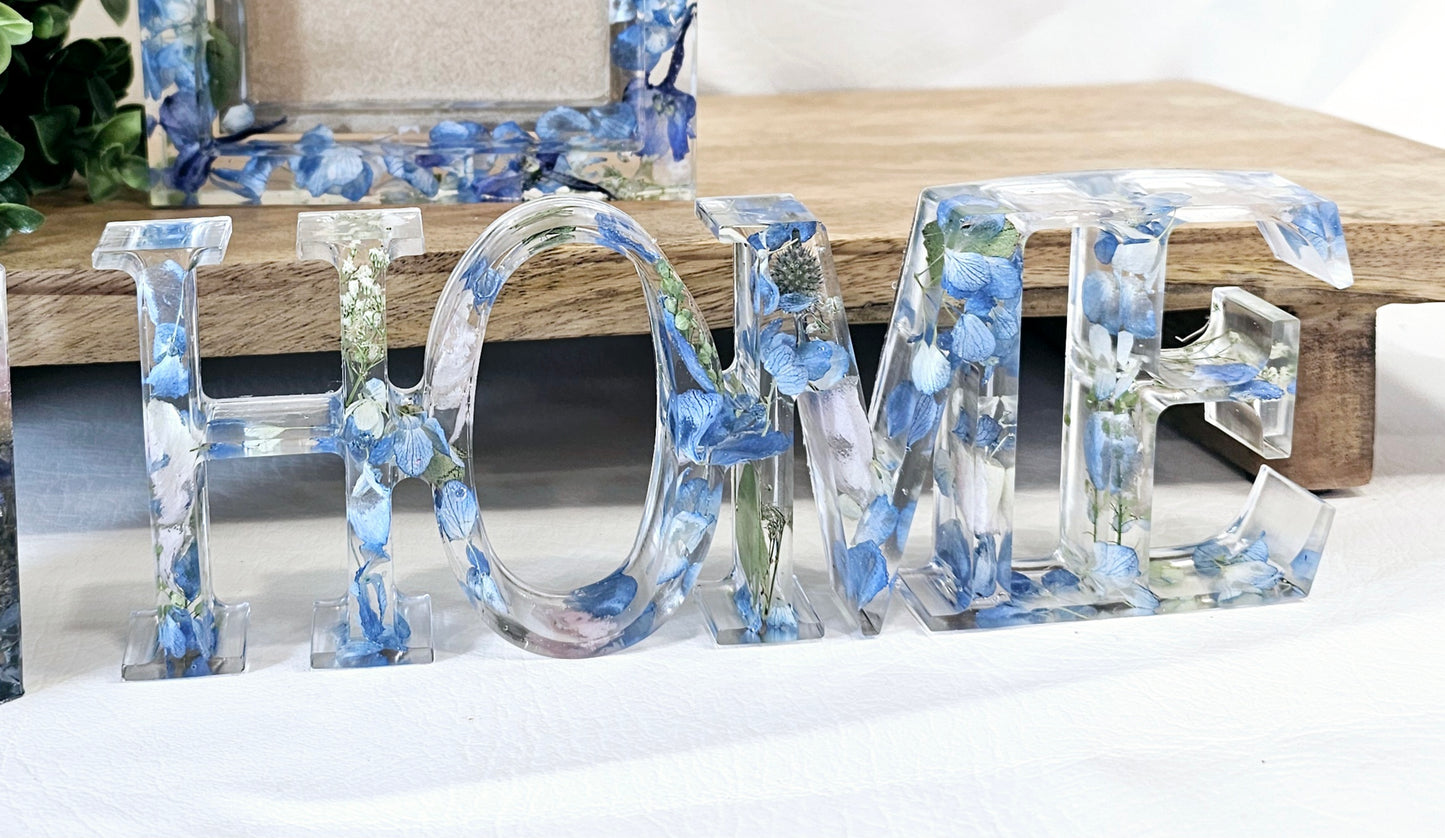 a clear resin ornament spelling home full of blue hydrangea 