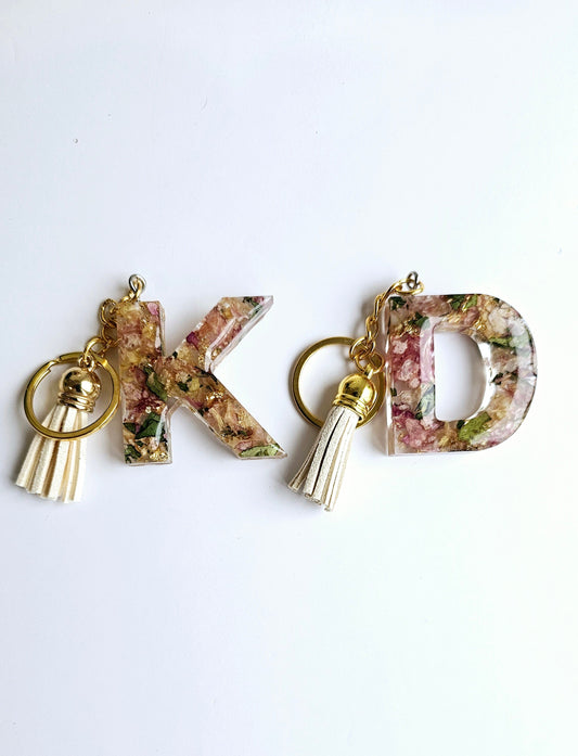 2 resin flower preservation keyrings in the initials K and D on a white background