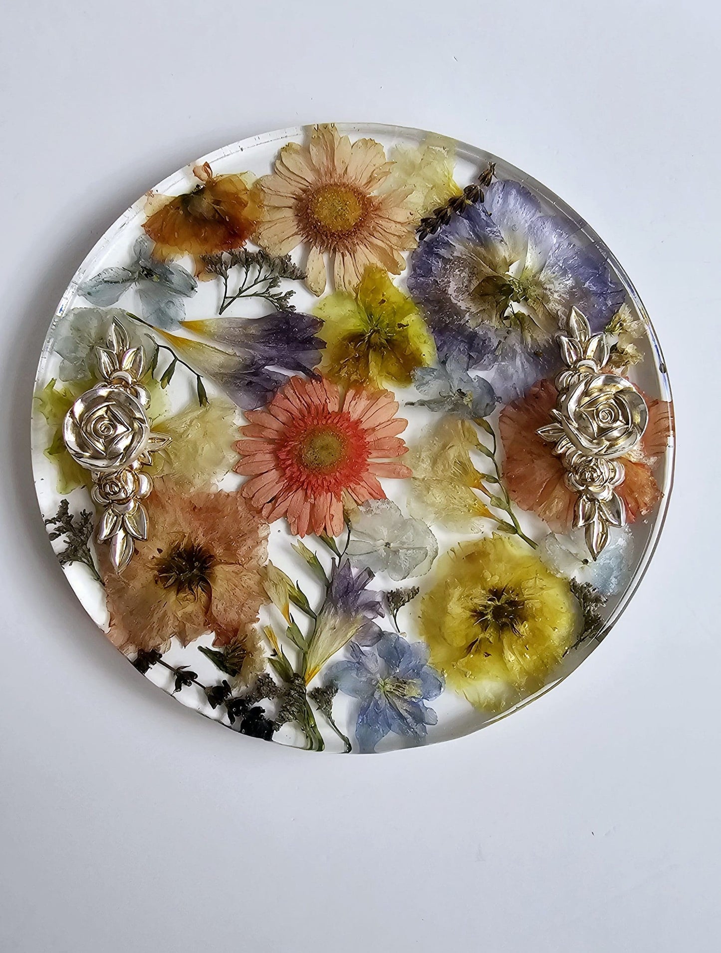 Round decorative plate with pressed flowers and gold leaf on a white background