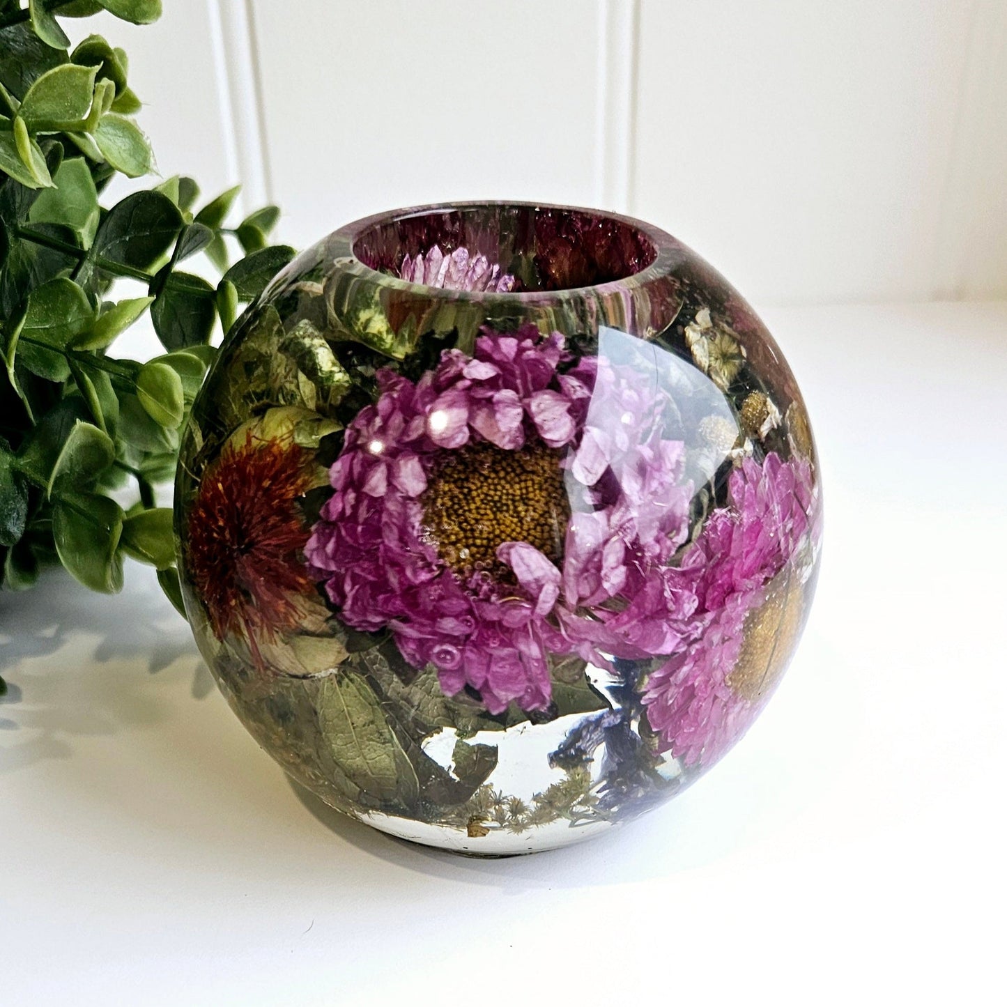 Round resin tealight holder with floral design on a white surface with greenery in the background