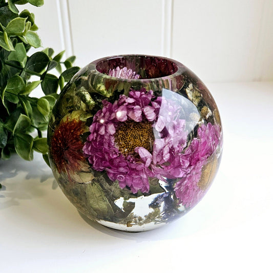 Round resin tealight holder with floral design on a white surface with greenery in the background
