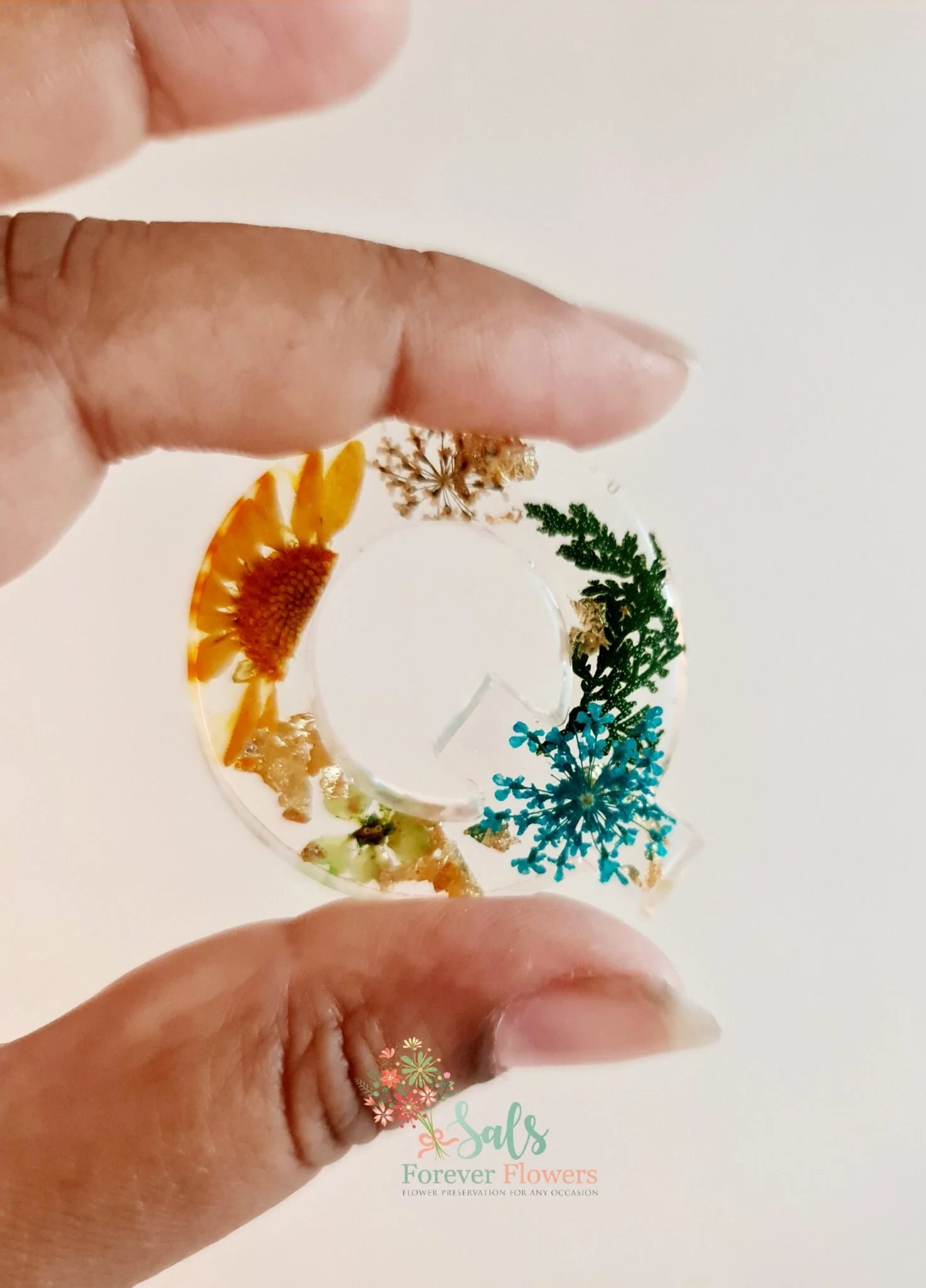 Hand holding a small round object with floral designs on a white background