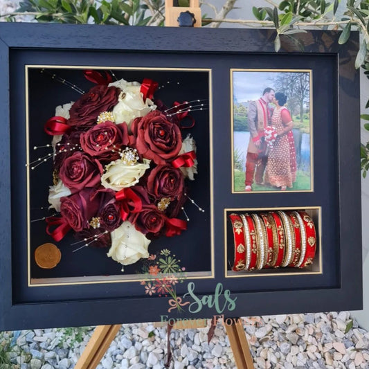 Framed display with red and white roses, a couple photo, and bangles on a stand.
