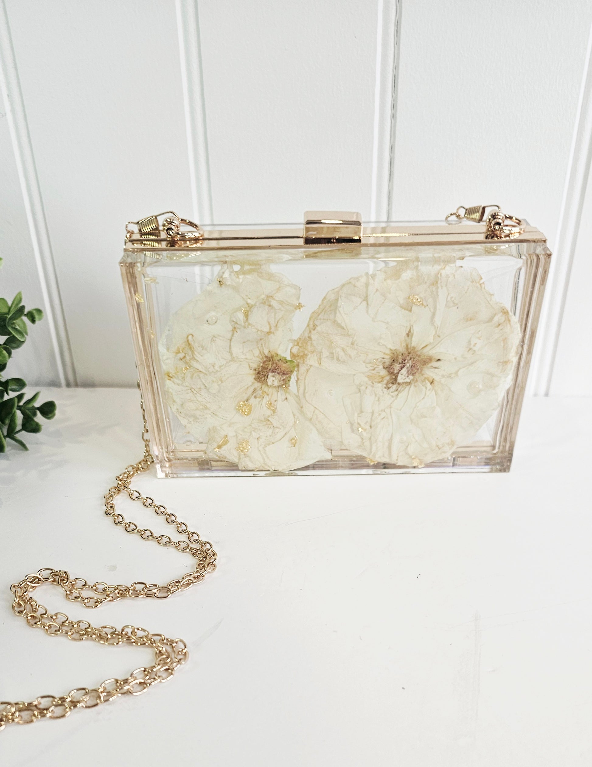Clear clutch with floral design and gold chain on a white surface