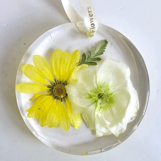 Round pendant with pressed yellow and white flowers on a white background