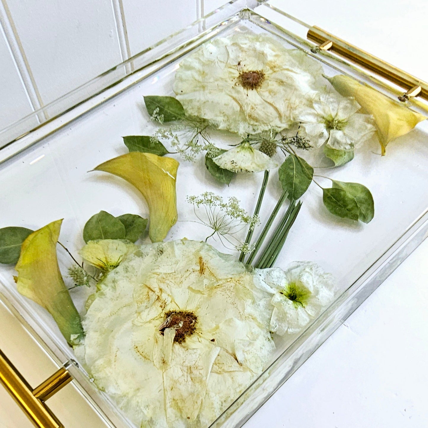 Clear resin tray with gold handles filled with flowers on a white surface.
