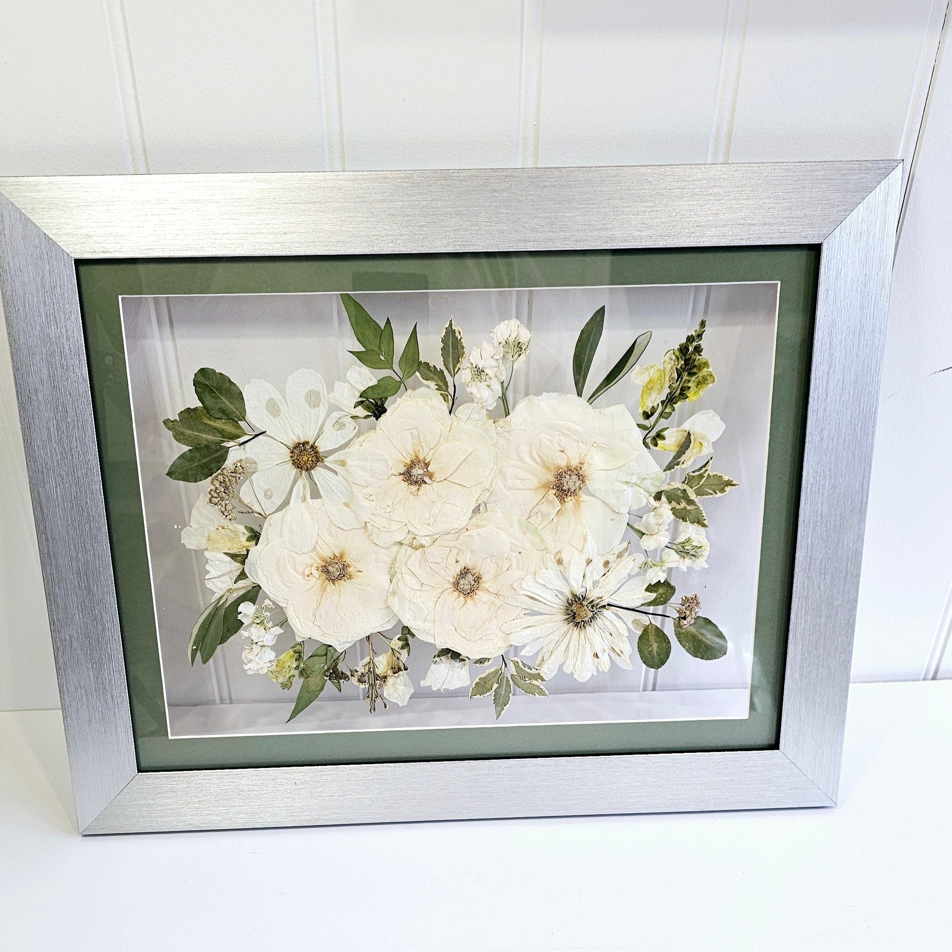 Framed arrangement of white flowers with green leaves on a white background