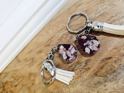 resin keychain with purple teardrop shaped charm and tassel on a wooden surface