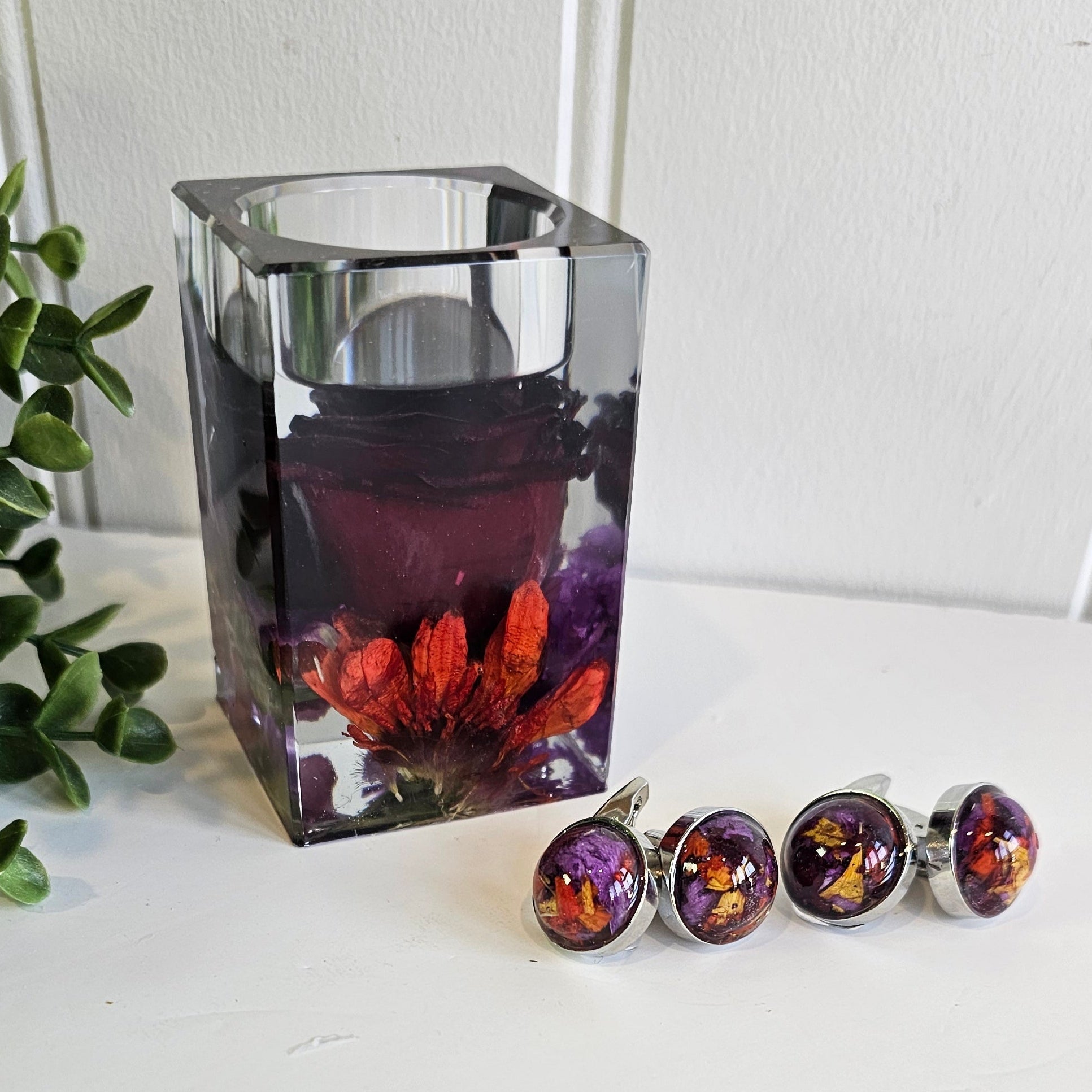 Decorative resin tealight holder with floral design on a white surface next to flower preservation cufflinks