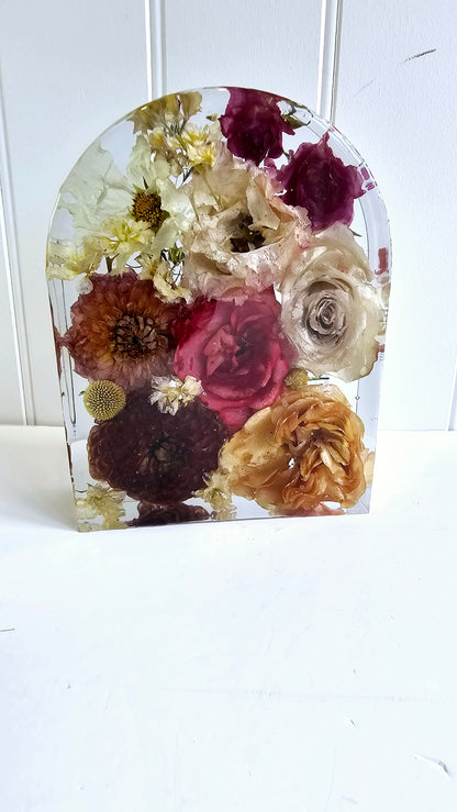 Decorative resin arch with pressed flowers in a clear resin block on a white background