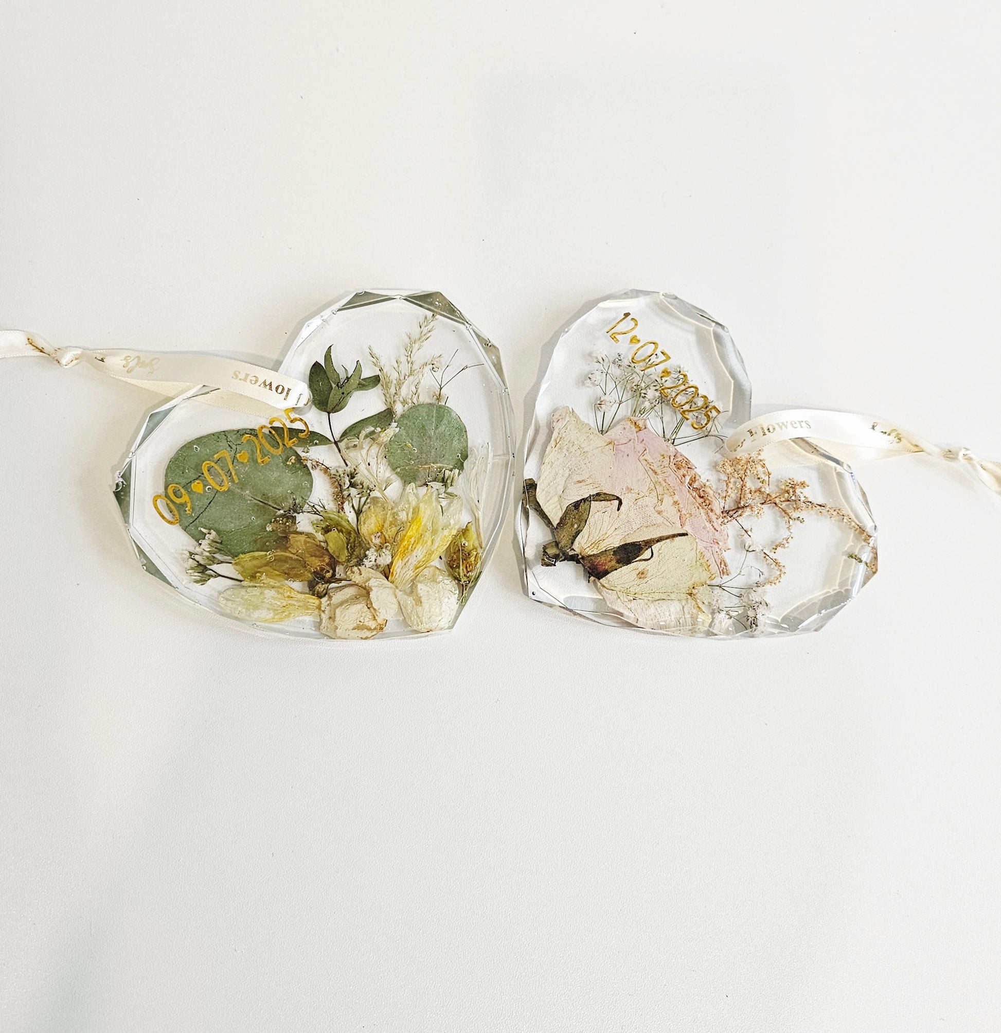 Heart-shaped resin pieces with pressed flowers and leaves on a white background