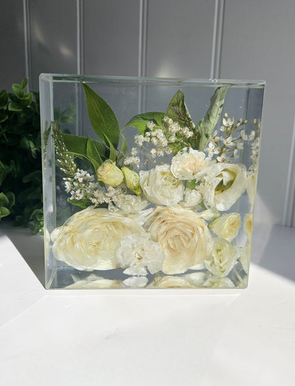 Clear resin block with preserved wedding  flowers in white and green leaves on a light gray background