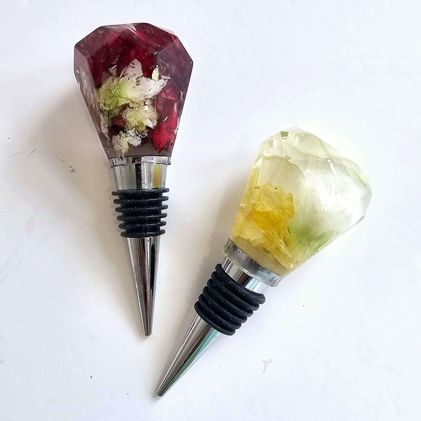 Two decorative wine bottle stoppers with gemstone-like tops on a white background