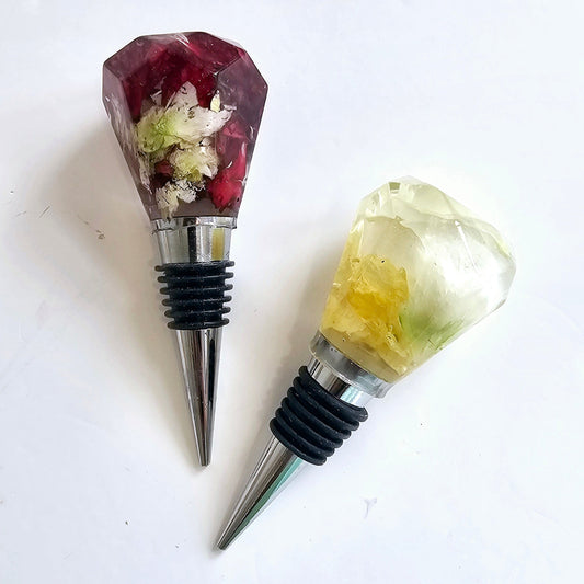 Two decorative wine bottle stoppers with gemstone-like tops on a white background