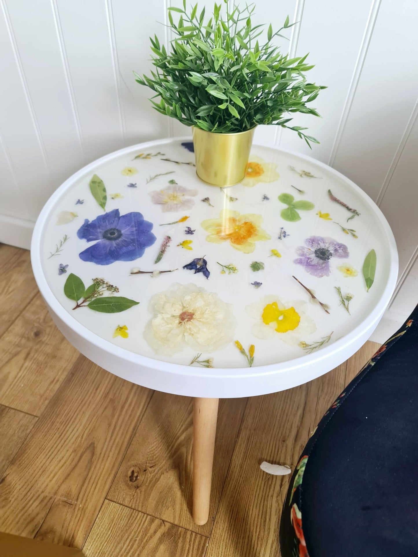 Round side table with floral design and a plant on top against a white wall.